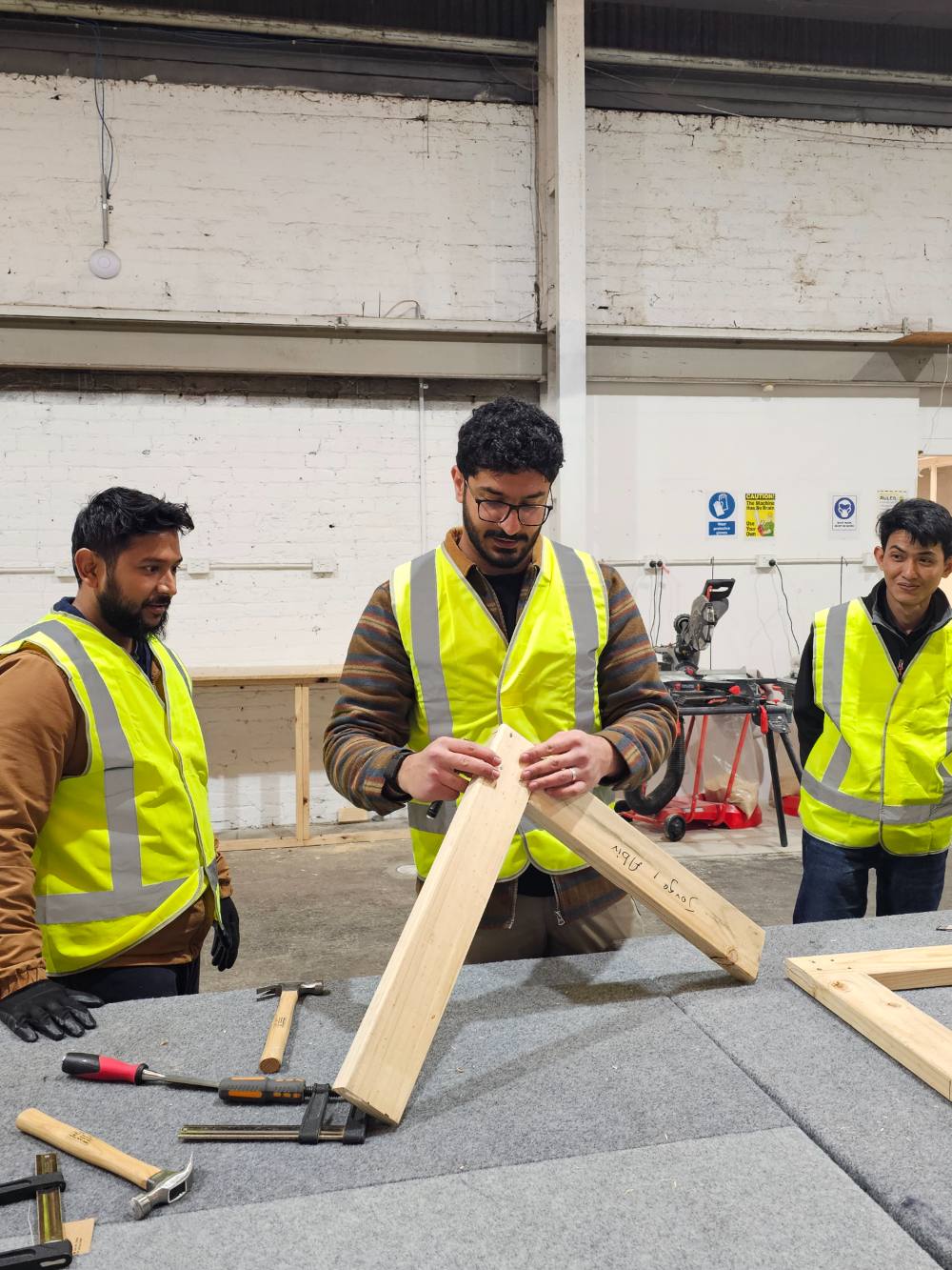 A trainer demonstrating a timber joint to two students at a workbench