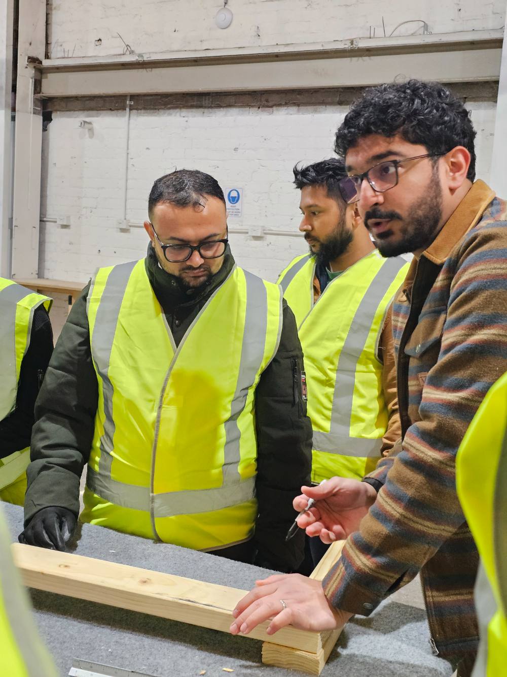 A trainer guiding students as they work on a piece of timber
