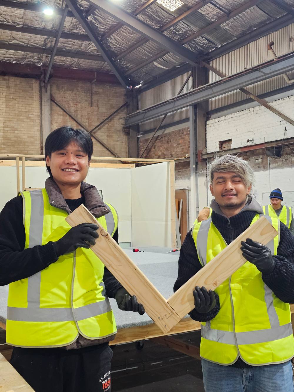 Two students in high-visibility vests holding a timber joint they made in the workshop