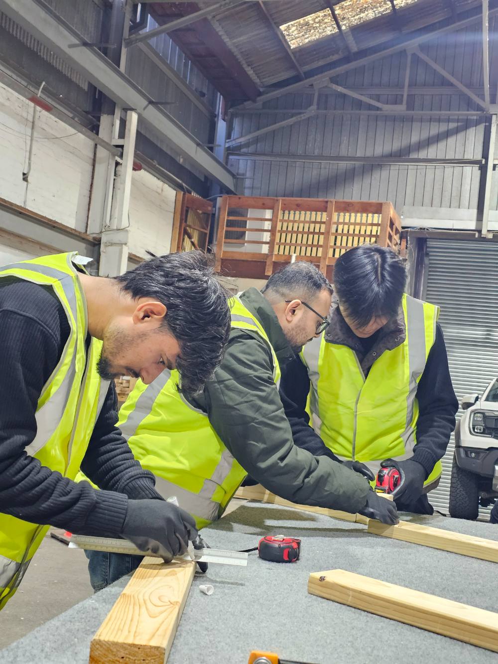 Three students measuring and marking out timber together at a workbench